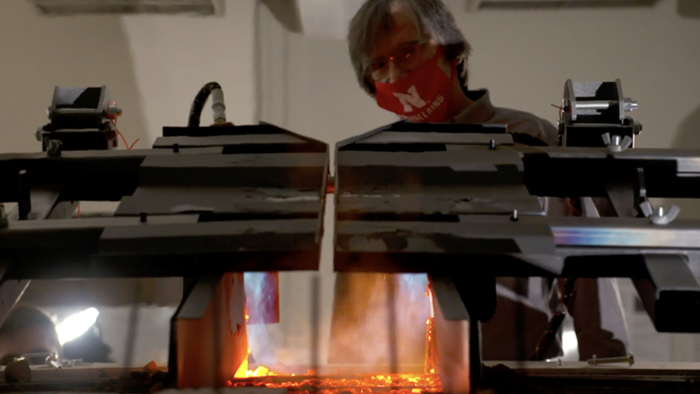 Steel testing machine clamps glowing metal under extreme heat in a laboratory setting.