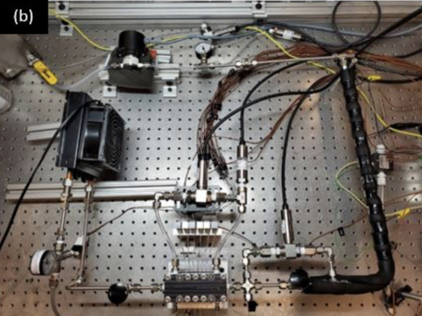 Experiment setup with interconnected pipes, wiring, gauges, and a fan on a perforated metal board.